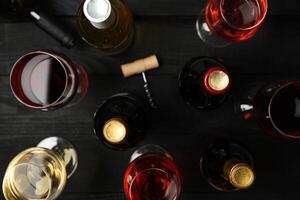 Bottles and glasses with different wine on wooden background, top view photo