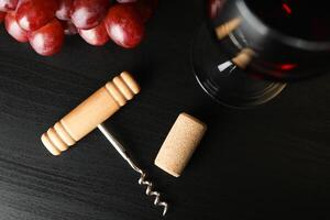 Grapes, corkscrew, cork and wine glass on dark table, top view photo