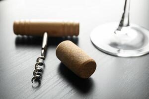 Corkscrew, cork and wine glass on dark table, close up photo