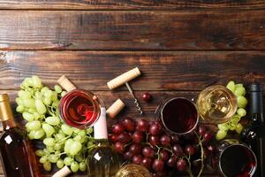 Flat lay. Grapes, corkscrew, bottles and glasses with wine on wooden table, copy space photo