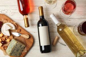 Grape, cheese, bottles and glasses with different wine on white wooden background, top view photo