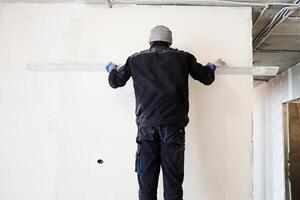 A construction worker plasters a concrete wall with a rule, skillfully leveling the surface to obtain an impeccable finish as part of a renovation project. photo