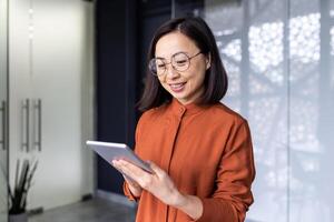 Smiling Asian young female programmer standing in office and working on tablet. photo