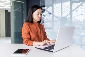 Young Asian female programmer, developer, tester is focused and serious sitting in the office and working on a laptop. photo