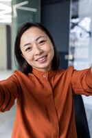 Vertical shot, call from office Asian business woman working inside modern office building, talking remotely with friends using app on phone for call. photo