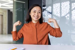 Portrait of happy successful Asian business woman, online meeting call, woman looking at camera smiling and holding hands up, super power and superhero gesture. photo