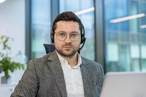 A man in a gray suit and headset looks directly at the camera, possibly working in a customer service or call center. photo