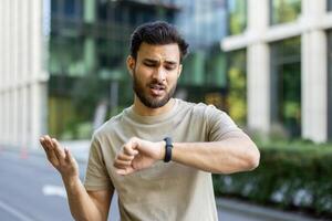 A young man looks at his watch while gesturing. Possibly running late, or tracking fitness activity during exercise. photo