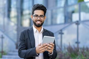 A young businessman in a smart suit engrossed in using his tablet computer. Captured outside a contemporary office setting, symbolizing global business and connectivity. photo
