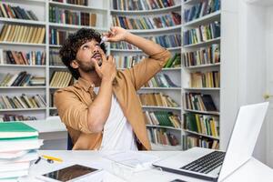 Concentrated islamic man with curly hair throwing head back while using eye drops and sitting in cabinet. Responsible male using prevention medicine for avoiding vision problems after work with pc. photo