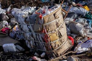 A large bundle of mixed waste materials is seen surrounded by scattered garbage in a landfill, highlighting serious pollution issues photo