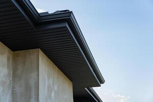 A detailed view of a building's rooftop with sleek metallic tiles and smooth lines against the blue sky, showcasing construction progress photo