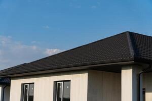 New metallic roof tiles installed on a residential building with windows, showcasing a contemporary design and clear skies photo