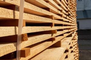 Sunlight highlights neatly arranged wooden planks in a construction yard, showcasing their texture and quality on a clear day photo