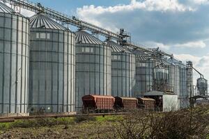 Grain silos at a farming site are filled with harvested crops as trucks wait for storage and transport beneath a partly cloudy sky photo