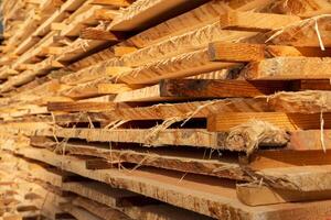 Stacked wooden planks showcase their natural textures and grains, illuminated by warm sunlight in a sawmill setting photo