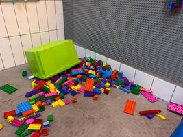 Brightly colored building blocks are spread across the floor near a green storage box, creating a playful mess in a children's play area photo