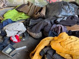 A pile of various clothing items lies on the ground in a dilapidated space, indicating neglect and lack of care in daylight hours photo