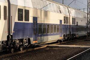 A sleek double-decker train is parked at the station, illuminated by warm late afternoon sunlight casting shadows on the tracks photo