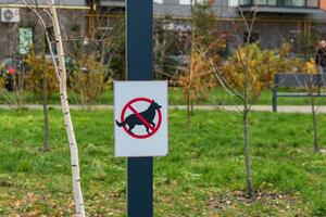 A clearly visible sign prohibits dogs in a park setting surrounded by trees and autumn leaves with a nearby walking path photo