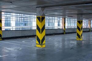 Underground parking garage features yellow caution pillars, clear parking markings, and an urban architectural backdrop with large windows photo