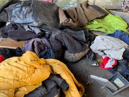 Piles of various types of clothing and blankets clutter an abandoned indoor area, showcasing neglect and disarray in the late afternoon light photo
