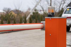 A barrier gate with an orange housing and flashing light stands at the entrance to a restricted area on a cloudy day, indicating controlled access photo