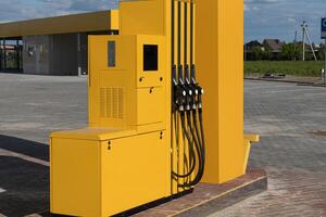 Fuel dispenser with multiple nozzles stands alone at a gas station, surrounded by open space and well-maintained surfaces under a clear sky photo