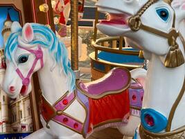 Two vibrant carousel horses with detailed designs stand ready for children at an amusement park, illuminated by the evening glow photo
