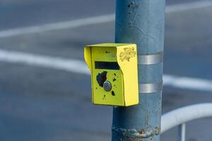 A bright yellow mail drop box is securely attached to a gray pole at a busy urban intersection under clear blue skies photo