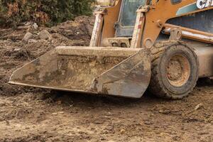 Heavy machinery works on earthmoving tasks at a construction site covered in mud and debris under overcast skies photo