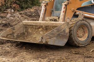 A skid steer loader is actively moving dirt and debris at a construction site on a cloudy day, showcasing the work in progress photo