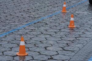 Three orange traffic cones are set on a slick cobblestone street, marking off a specific area likely for parking or roadwork photo