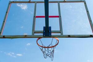 A weathered basketball hoop and net are positioned against a bright blue sky, showcasing a peaceful afternoon atmosphere photo