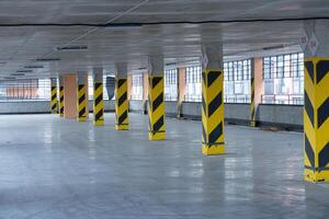 Spacious parking garage features yellow and black striped columns, large windows allowing natural light, and a clean concrete floor photo