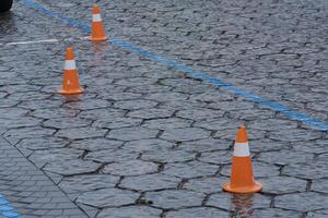 Orange traffic cones sit on a wet cobblestone surface, marking no parking zones and creating safety measures in rainy conditions photo