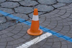 A traffic cone stands next to worn pavement featuring blue lines, indicating a potential construction area or restricted zone in the city photo