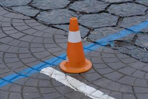 An orange traffic cone stands on patterned pavement with blue and white markings, indicating a construction area in a city environment photo