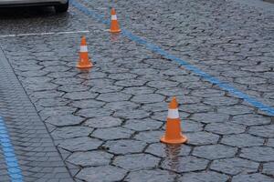 Wet pavement in an urban parking lot features orange cones spaced evenly, indicating reserved spaces during a rainy day photo