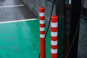 Striped poles stand near a charging station on vibrant green pavement in an urban setting, with rain-soaked tiles indicating recent weather photo