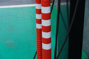 Two red and white striped poles stand next to a green pavement, with power cables nearby, capturing an urban, busy atmosphere photo