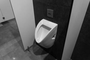 A urinal is installed in a contemporary restroom with gray tiles and a simple aesthetic that emphasizes cleanliness and functionality photo