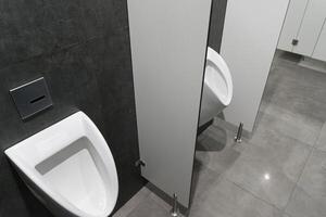 A contemporary restroom showcases a white urinal beside closed privacy stalls, all set against dark gray walls and tiled flooring photo
