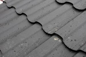 Dark roof tiles are covered with droplets of rainwater after a light rain in a city during the afternoon, showcasing the weather effects on roofing photo
