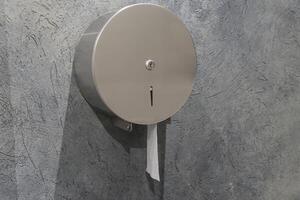 A stainless steel tissue dispenser is securely mounted to a textured gray wall in a public restroom, providing easy access for users photo
