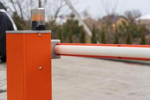 A bright orange barrier gate stands at the entrance of a parking lot, with a flashing light indicating restricted access to vehicles photo