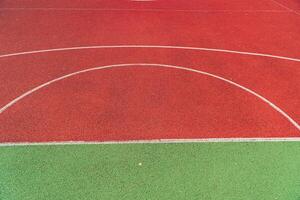 A basketball court surface features striking red and green areas, with clear markings visible under bright afternoon sunlight photo