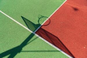 Brightly colored basketball court features a shadow of the hoop and backboard on a sunny afternoon, inviting players to enjoy the sport photo