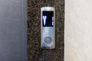 A stylish elevator control panel features a digital display, glowing with blue lights, set against a sleek stone wall in an upscale building photo