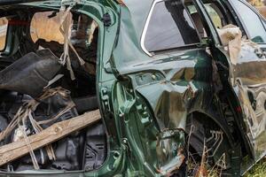 Metal crumpled and torn, the remains of a vehicle rest forgotten in a field, stark evidence of a recent accident amid nature's quiet photo